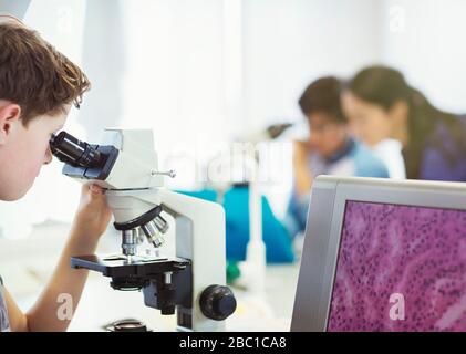 Boy student using microscope, conducting scientific experiment in laboratory classroom Stock Photo