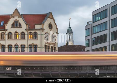 Germany, Hamburg, Blurred motion of elevated train passing residential building with tower of Saint Michaels Church in background Stock Photo
