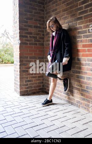 Young woman with leg prosthesis standing at a brick wall Stock Photo
