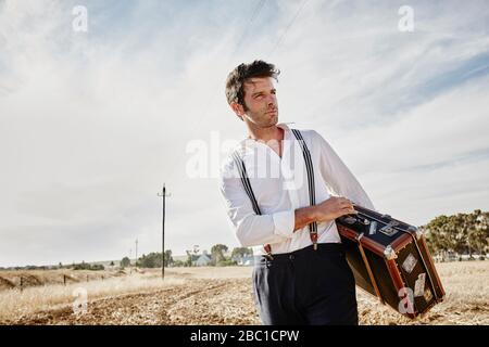 Man in old-fashioned clothes with suitcase in the countryside Stock Photo