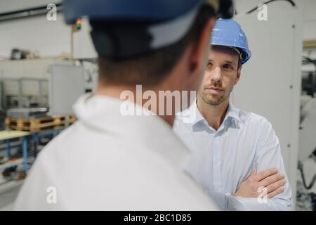 Two men wearing hard hats talking in a factory Stock Photo