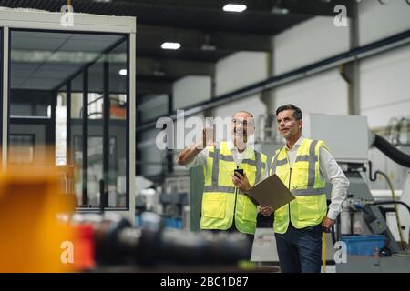 Two men in reflective vests talking in a factory Stock Photo