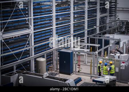 Supervisor and workers discussing information hanging on wall in factory Stock Photo