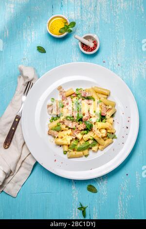 Italian recipe Pasta tortilloni with green pea, mint leaves, cheece, smoked bacon and cheese. Top view, blue background. Stock Photo