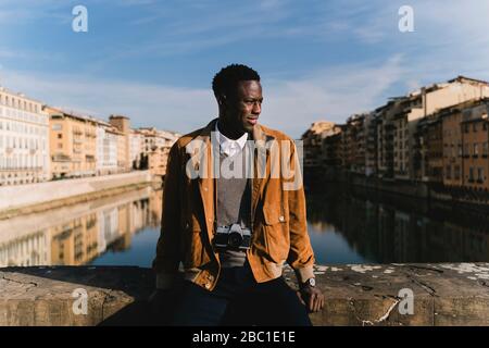 Young man with a camera on a bridge above river Arno, Florence, Italy Stock Photo