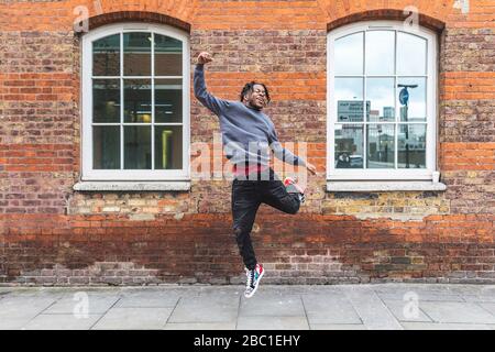 Young man jumping in front of brick wall Stock Photo