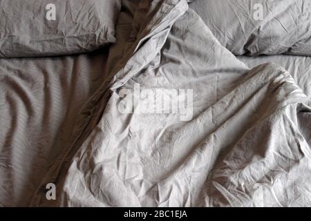 Morning empty messy bed gray bed linen, bedclothes. Sheet, blanket, pillows and wooden headboard. Stock Photo