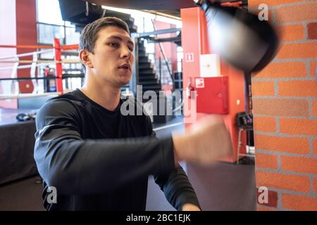 Young man exercising at punch bag in boxing club