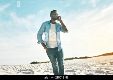 Young man talking on cell phone on sunny beach Stock Photo
