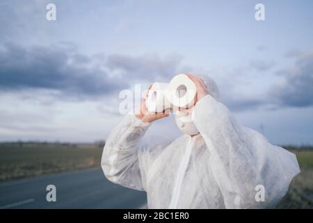 Man wearing protective suit and mask using toilet rolls like binoculars Stock Photo