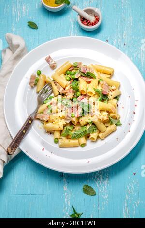 Italian recipe Pasta tortilloni with green pea, mint leaves, cheece, smoked bacon and cheese. Top view, blue background. Stock Photo