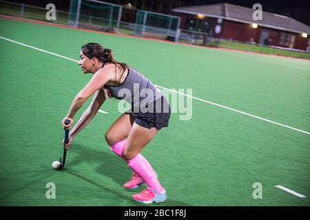 Determined young female field hockey player playing on field at night Stock Photo