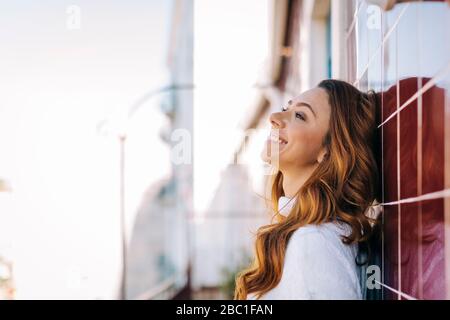 Happy young woman leaning against a tile wall