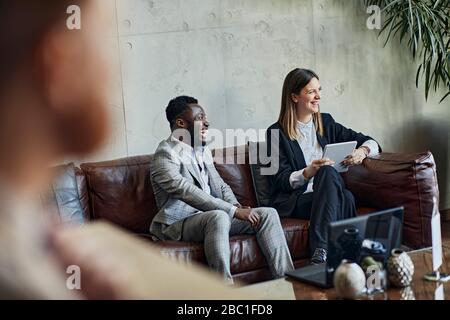 Laughing businessman and businesswoman sitting on couch in hotel lobby during a meeting Stock Photo