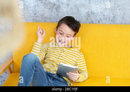 Boy playing with tablet on yellow couch Stock Photo