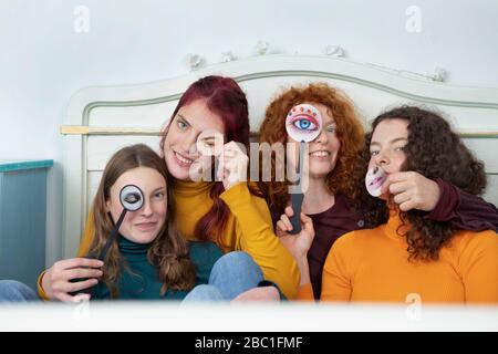 Family portrait of mother and her three daughters sitting together on bed holding paper masks Stock Photo