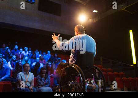 Audience watching male speaker in wheelchair talking on stage Stock Photo