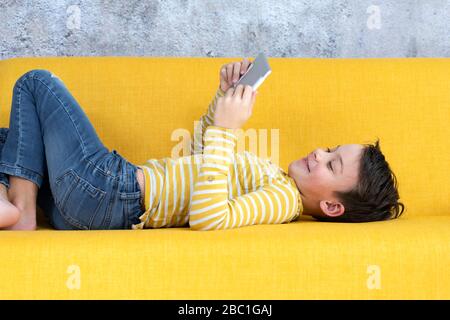 Boy playing with tablet on yellow couch Stock Photo