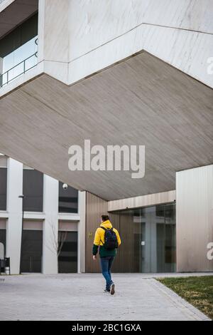 Rear view of man with backpack walking along building in the city Stock Photo