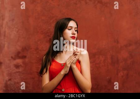 Close up portrait of young woman with red dress in front of red urban wall in Seville, Spain Stock Photo