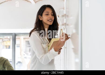 Portrait of woman writing on whiteboard in office Stock Photo