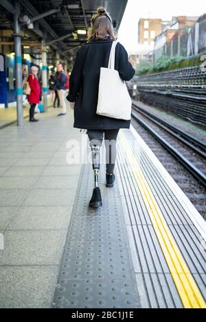 Rear view of young woman with leg prosthesis walking at station platfom Stock Photo