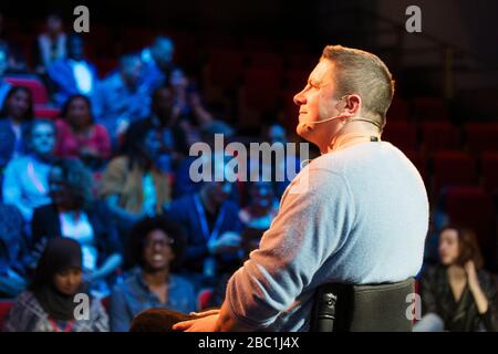 Smiling male speaker in wheelchair on stage Stock Photo