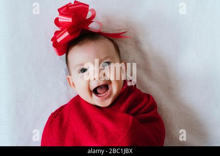 Portrait of happy baby girl with red ribbon on her head wrapped in red blanket Stock Photo