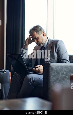 Businessman using laptop and smartphone in hotel lobby Stock Photo
