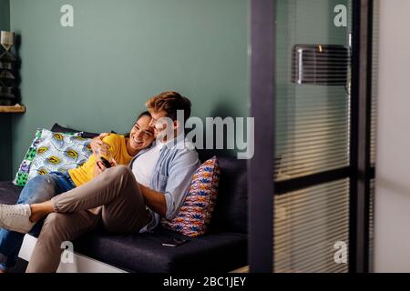 Happy affectionate young couple sitting on the couch at home Stock Photo