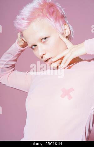 Portrait of young woman with short pink hair wearing pink top in front of pink background Stock Photo