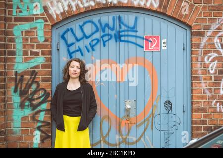 Portrait of brunette woman standing in front of a brick wall with an old gate and graffiti