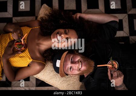 Portrait of happy couple lying on the floor drinking fresh ice tea Stock Photo
