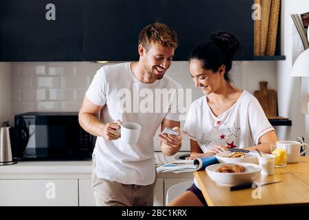 Happy young couple in the kitchen looking at cell phone Stock Photo