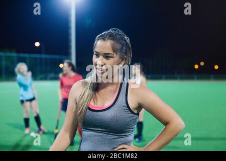 Tired young female field hockey player resting on field at night Stock Photo