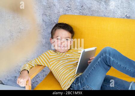 Boy playing with tablet on yellow couch Stock Photo