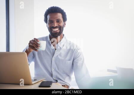 Portrait smiling, confident businessman drinking coffee at laptop Stock Photo