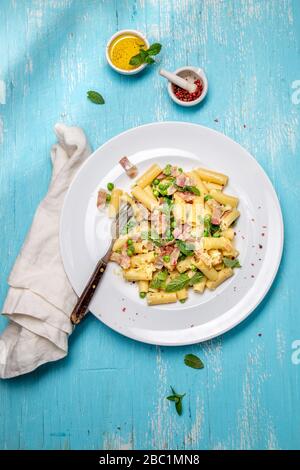 Italian recipe Pasta tortilloni with green pea, mint leaves, cheece, smoked bacon and cheese. Top view, blue background. Stock Photo