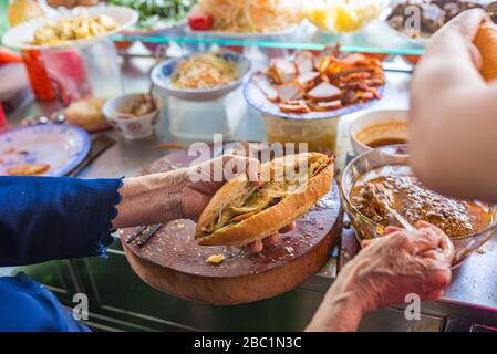 Woman selling street food Banh Mi at vendor in Vietnam Stock Photo