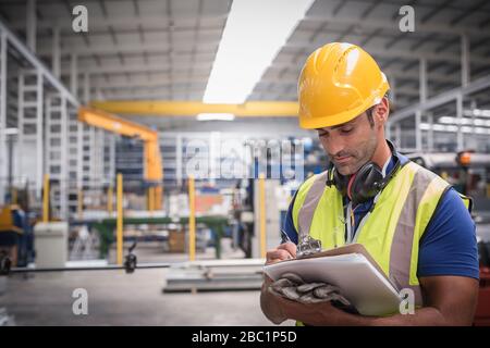 Male worker writing on clipboard in factory Stock Photo