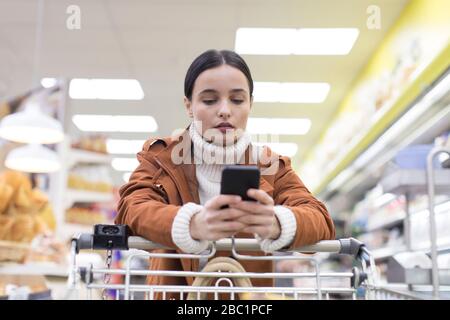 Young woman with smart phone shopping in grocery store Stock Photo