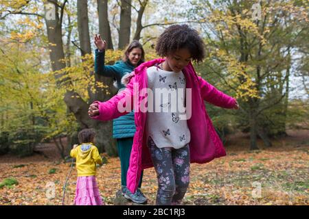 Mother and daughters balancing on fallen log in autumn woods Stock Photo