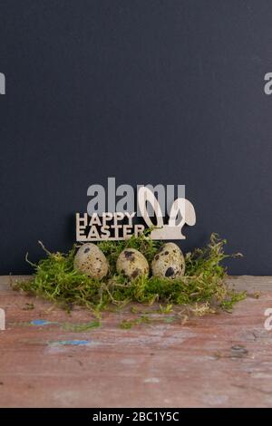 Quail eggs stand in a nest of green moss next is a sign of the Happy Easter. Top views Stock Photo