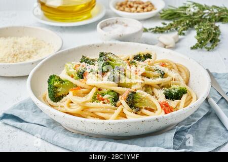 Spaghetti pasta with broccoli, bucatini with peppers, garlic, pine nuts. Light white table. Stock Photo