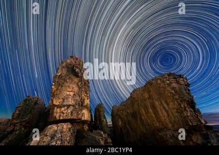 A beautiful night sky photograph with circular star trails against a deep blue sky with majestic dramatic rocks in the foreground, taken in the Cederb Stock Photo
