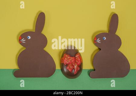Chocolate easter bunnies with chocolate painted icing eggs on a green-yellow background with copy space. Happy easter. Stock Photo