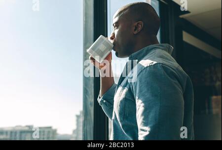 Young man having coffee in modern office. businessman standing by window in office drinking coffee. Stock Photo