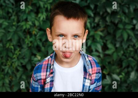 Naughty boy sticks out tongue outdoors in park Stock Photo