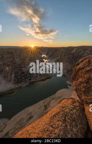 A beautiful vertical landscape view of the Augrabies Falls Gorge, mountains and river in South Africa, taken at sunset with a sunburst on the horizon Stock Photo