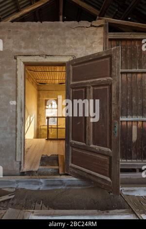 A vertical photograph inside an abandoned house, with an open door framing another room, taken in the ghost town of Kolmanskop, Namibia. Stock Photo